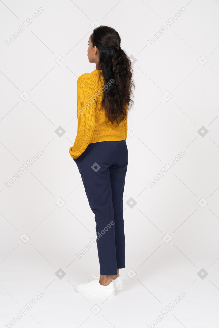 Vista lateral de una niña en ropa casual de pie con la mano en el bolsillo