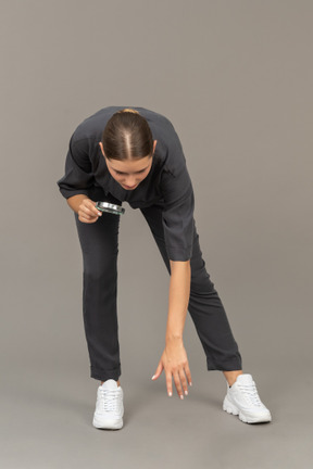 Front view of a young woman in a jumpsuit holding a magnifying glass