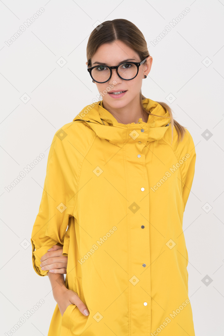 Girl in yellow coat and glasses with one hand holding another one kidden in the pocket