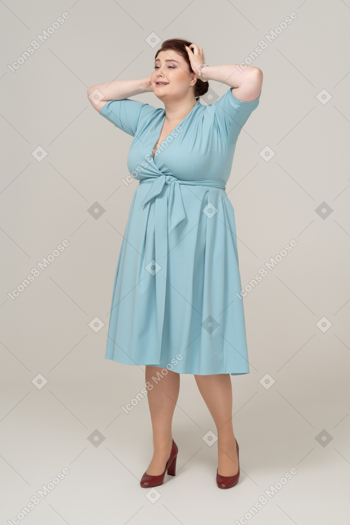 Front view of a woman in blue dress posing with hands on head