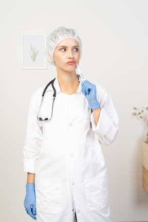 Vista frontale di una giovane dottoressa perplessa con lo stetoscopio che tiene il termometro