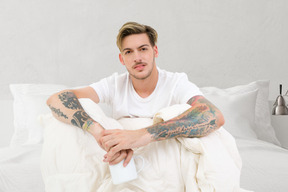 Giovane uomo tatuato seduto nel suo letto
