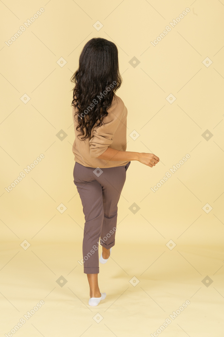 Back view of a dark-skinned walking young female