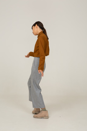 Vista lateral de uma jovem mulher asiática de calça e blusa fazendo uma reverência