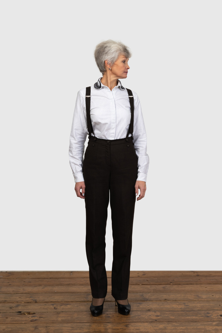 Front view of an old female in office clothes standing still indoors looking aside