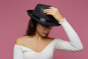 Front view of a mysterious lady hiding her face and holding black hat