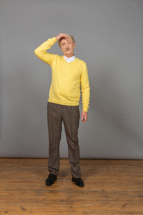 一个困惑的老人摸头，穿着一件黄色的套衫的前视图