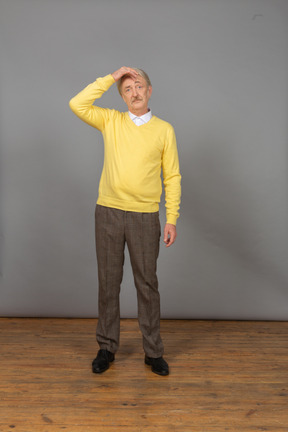 Front view of a confused old man touching head and wearing a yellow pullover