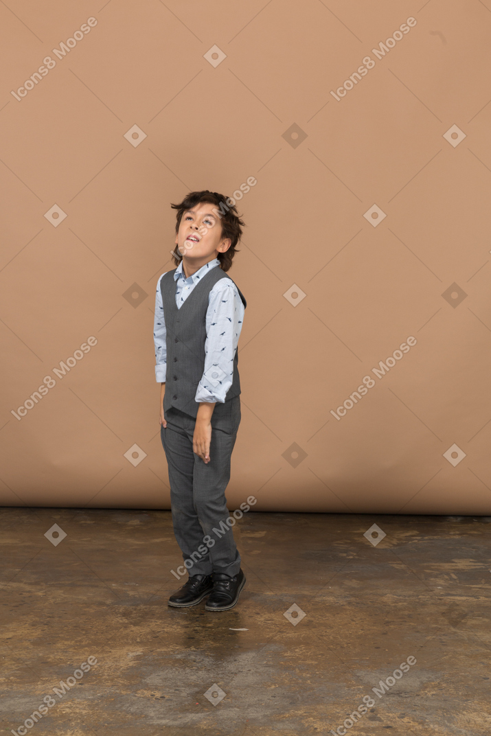 Vista frontal de un chico lindo en traje mirando hacia arriba