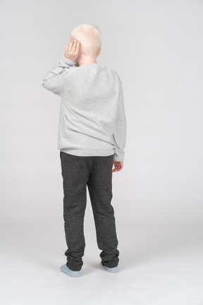 Vista traseira de um menino colocando a palma da mão no ouvido