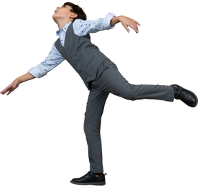 Side view of a boy in suit balancing on one leg with outstretched arms
