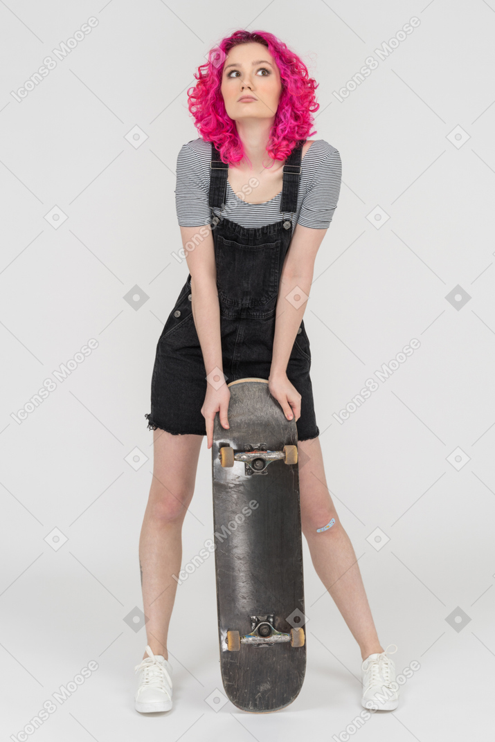 Une fille aux cheveux rose s'appuyant sur une planche à roulettes