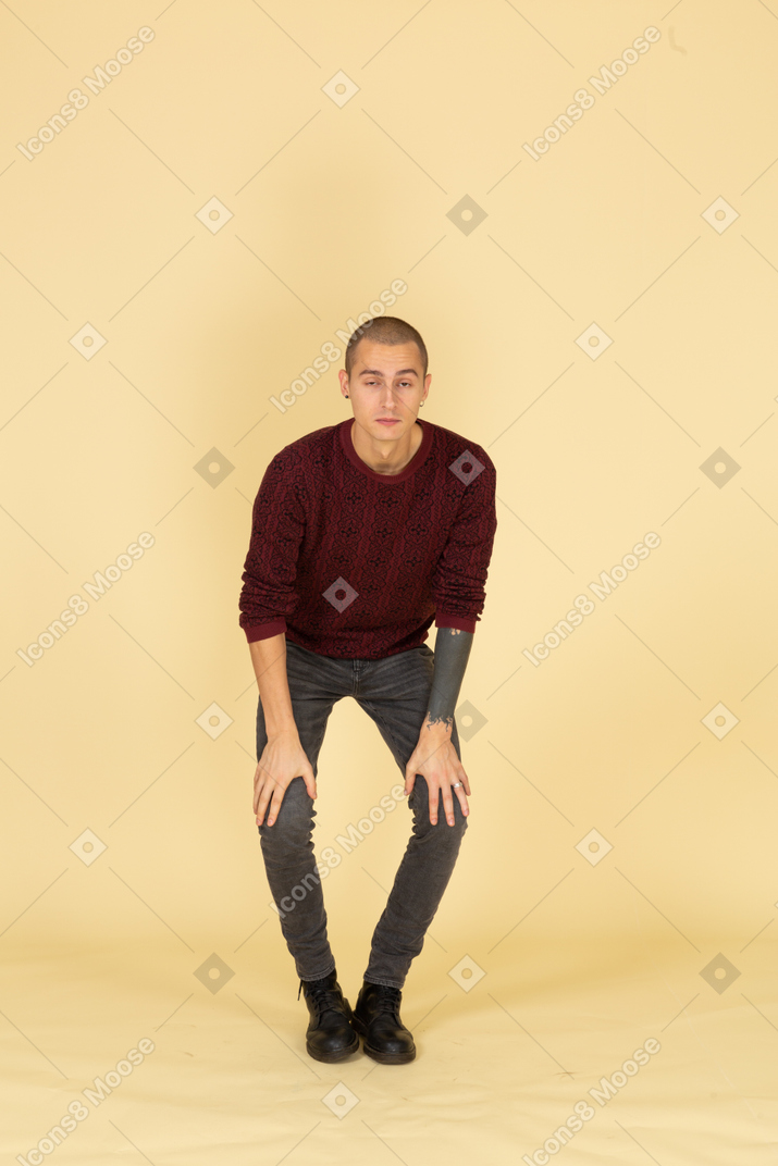 Vue de face d'un jeune homme sérieux se penchant en avant et mettant les mains sur les jambes