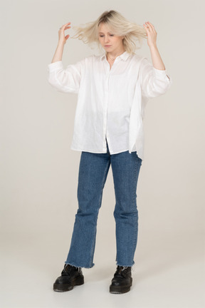 Front view of a blonde female touching her messy hair and looking down