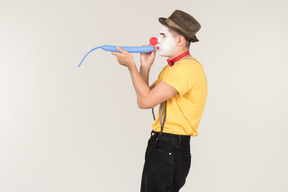 Male clown standing in profile and blowing a balloon