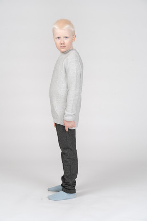 Vista lateral de un niño chico en ropa casual mirando a la cámara
