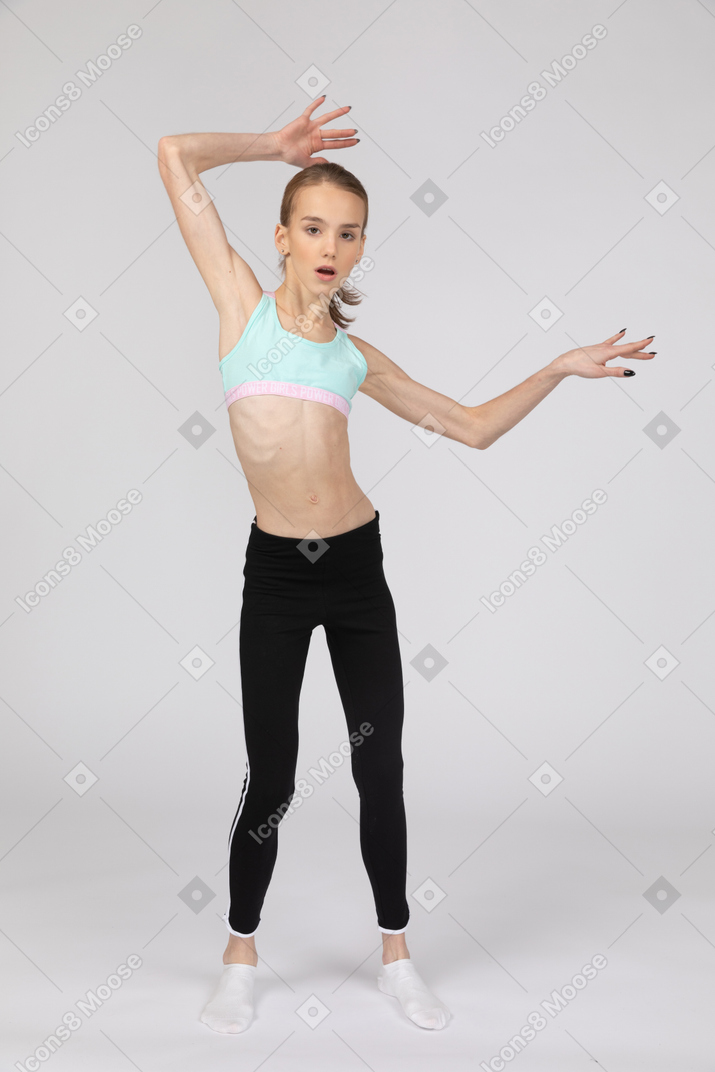 Vista frontal de una jovencita en ropa deportiva levantando las manos y abriendo la boca