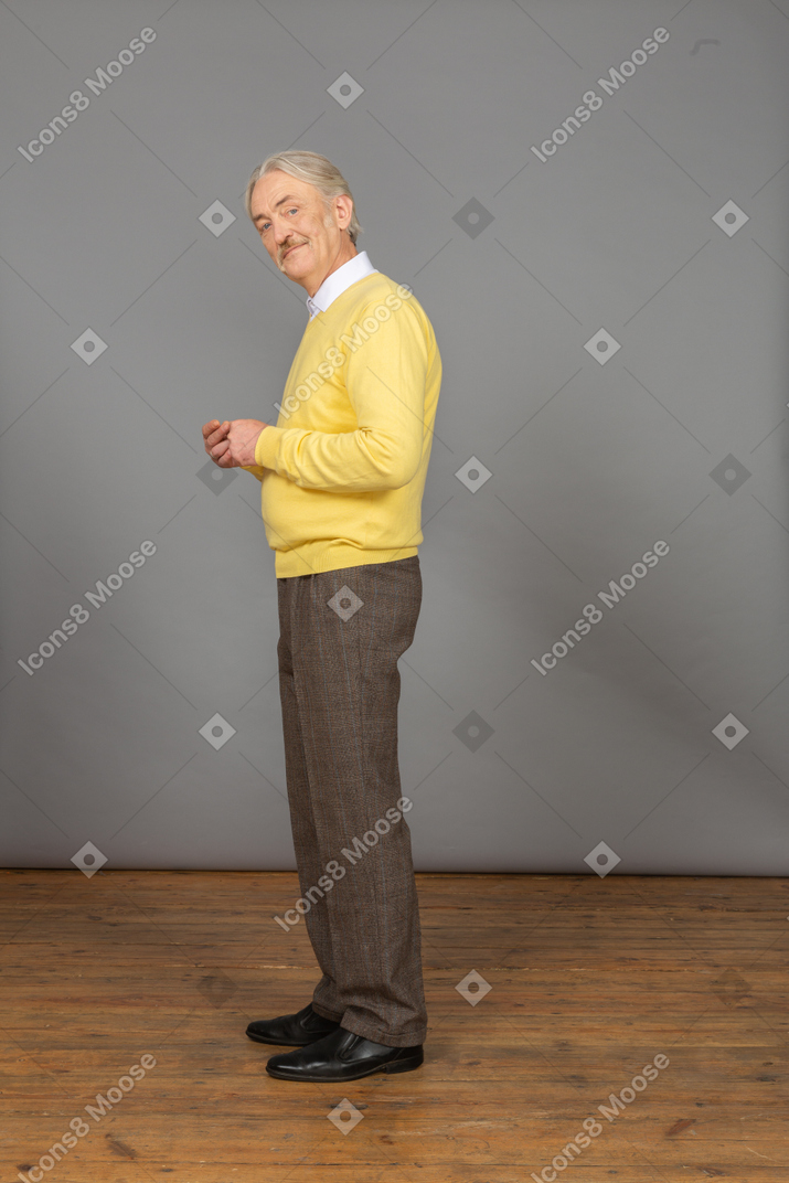 Vista lateral de um homem sorridente, vestindo uma camisola amarela, juntando as mãos e olhando para a câmera