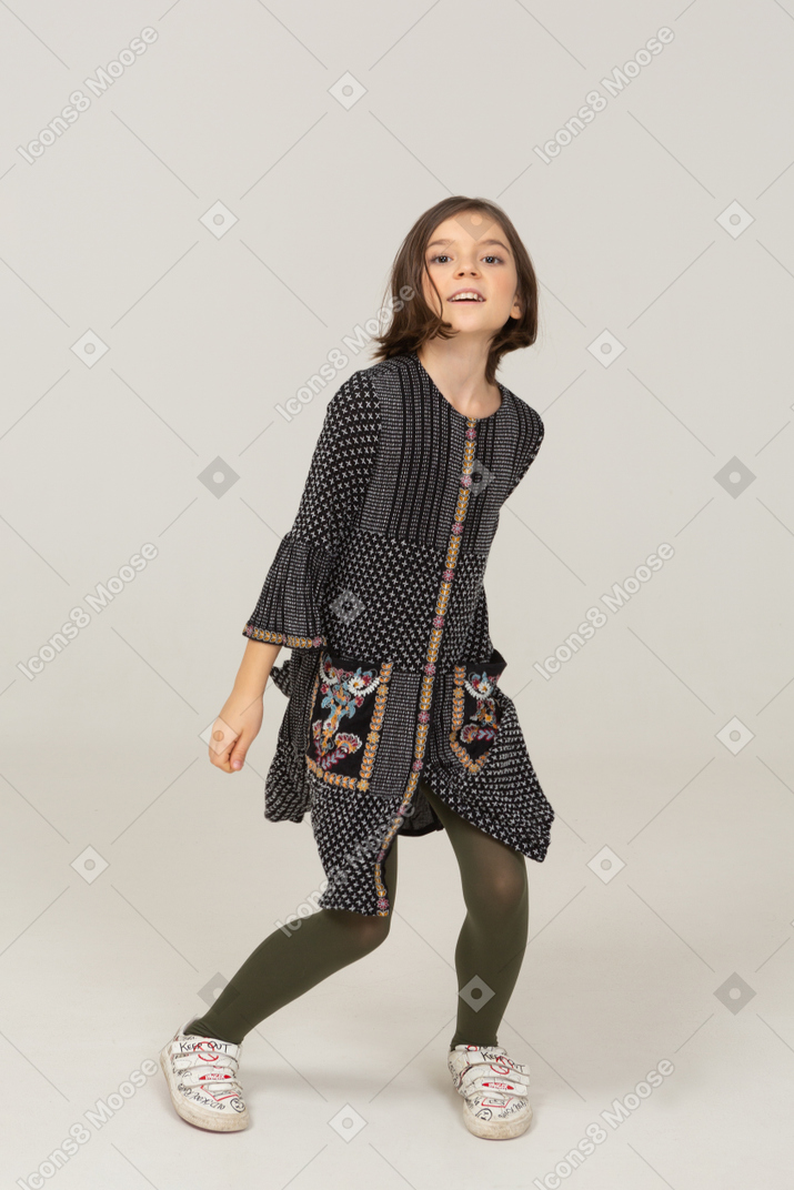 Vista frontal de una niña saltando en vestido extendiendo las manos y las piernas