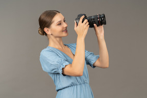 Vista de três quartos de uma jovem sorridente com vestido azul tirando uma foto