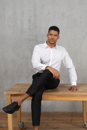 Confident man in formal clothes sitting cross legged on a table