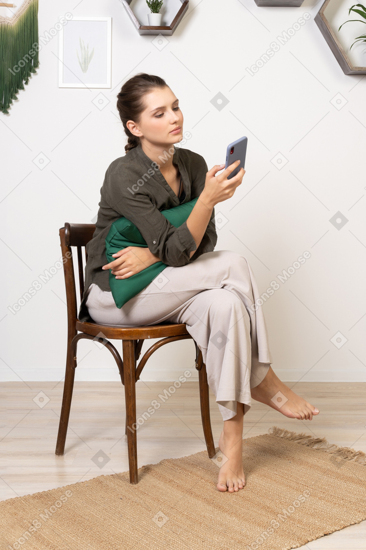 Front view of a bored young woman sitting on a chair while checking her phone