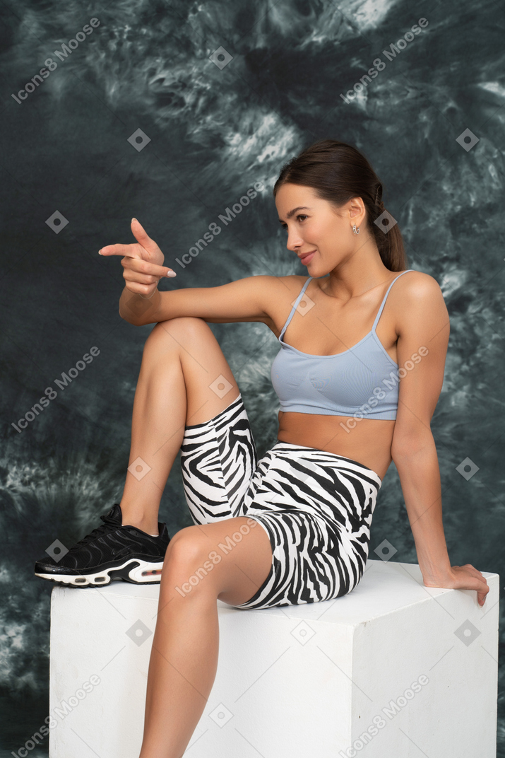Positive female athlete gesticulating sitting on a cube