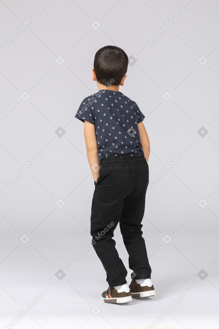 Vista traseira de um lindo menino em roupas casuais, posando com as mãos nos bolsos
