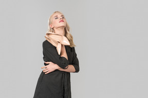 Eine junge, blonde person in einem schwarzen kleid und beige high heels in ihren händen, die vor einem schlichten grauen hintergrund stehen