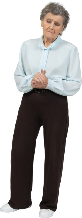 Vista frontal de una anciana disgustada en blusa y pantalones cogidos de la mano