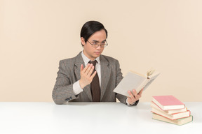 An asian teacher in a checkered suit, a tie and a book in his hand, working with the class