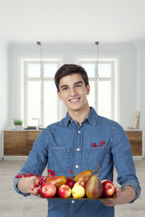 Homem bonito segurando a bandeja cheia de frutas