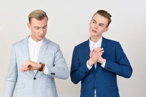 Man looking at watch and his male colleague looks pensive