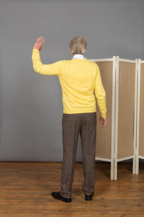 Back view of an unrecognizable old man raising his hand
