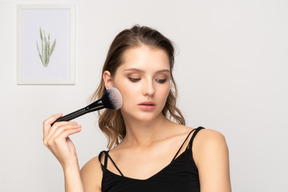 Vue de face d'une jeune femme sensuelle tenant un pinceau de maquillage