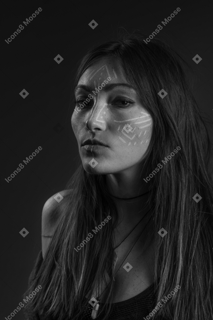 Noir ritratto di tre quarti di una giovane donna con arte facciale etnica che guarda tristemente da parte