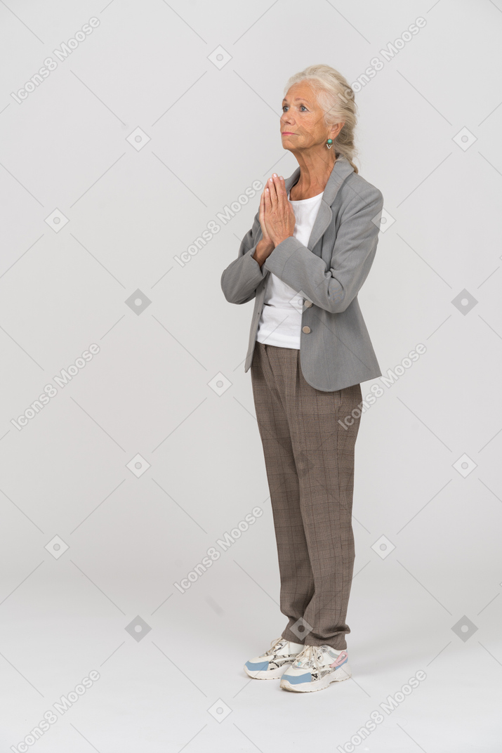 Вид сбоку пожилой дамы в костюме, делающей молитвенный жест
