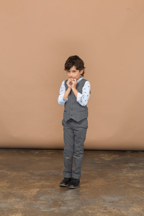 Vista frontal de un niño con traje gris haciendo un gesto de oración