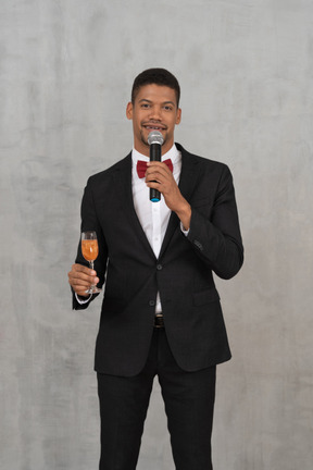 Vista frontal del hombre con micrófono y copa de champán mirando a la cámara