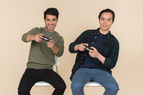 Interracial friends sitting in chairs and playing video games