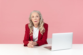 Mujer elegante envejecida sentado en el escritorio de la computadora de oficina