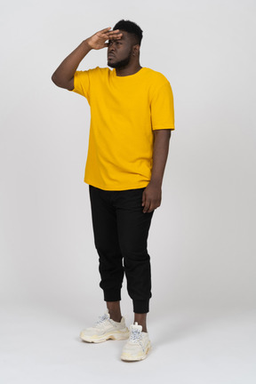 Vista di tre quarti di un giovane uomo dalla pelle scura in maglietta gialla che cerca qualcosa