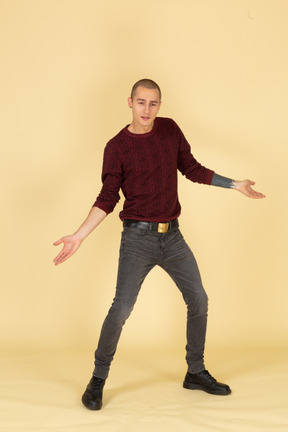 足と腕を広げて立っている赤いプルオーバーの若い男の正面図
