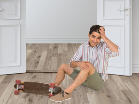 A man sitting on the floor next to a skateboard
