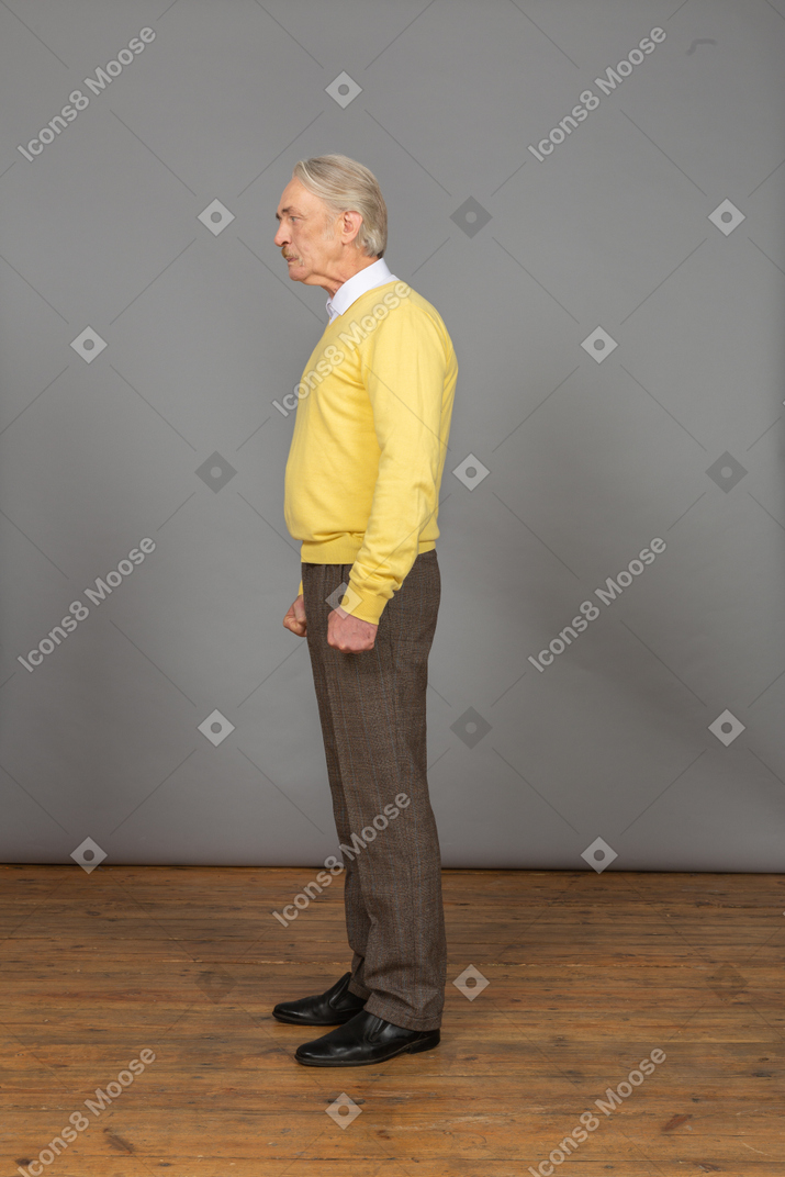 Side view of an old mad man in yellow pullover clenching fists