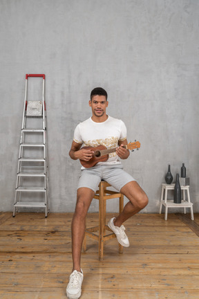 Front view of a man on a stool playing ukulele