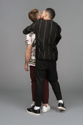 Back view of a young man hugging another passionately from the back