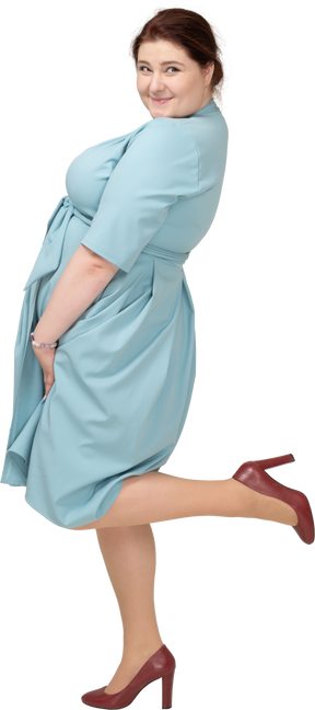 Vista lateral de uma mulher de vestido azul em pé sobre uma perna