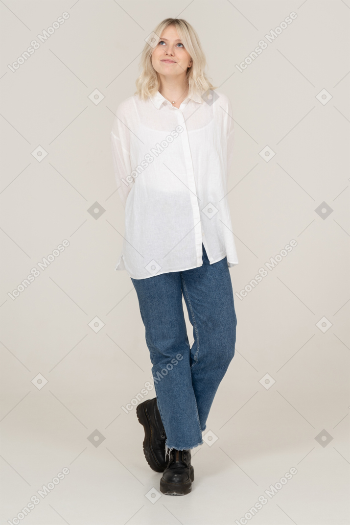 Front view of a shy blonde female in casual clothes crossing legs and looking up