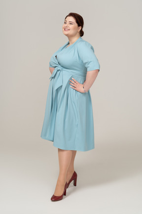 Vista lateral de uma mulher feliz em um vestido azul em pé com as mãos nos quadris